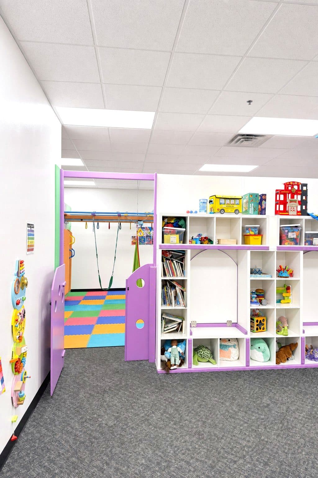 A playroom at our Eagan clinic with a swing frame, colorful floor tiles, and shelves of toys